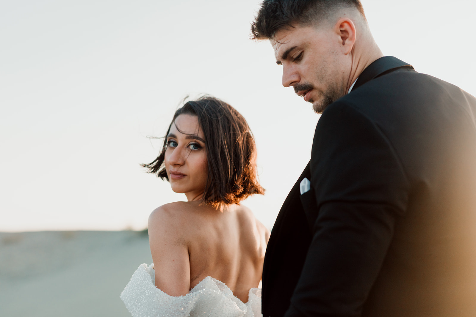 Bride looking back over her bare shoulder beside the groom on the dunes