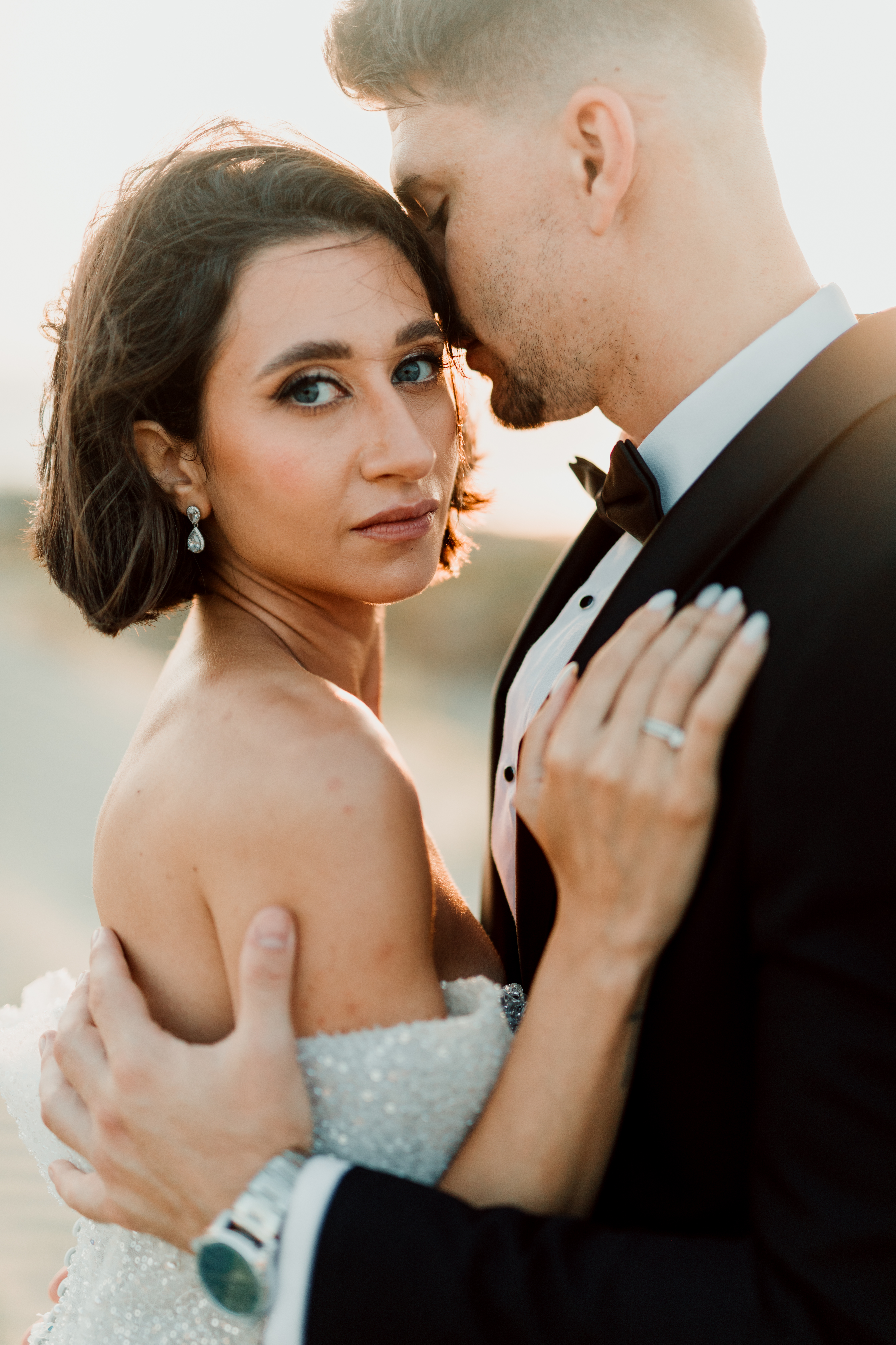 Bride looking to camera while resting against the groom in warm evening light