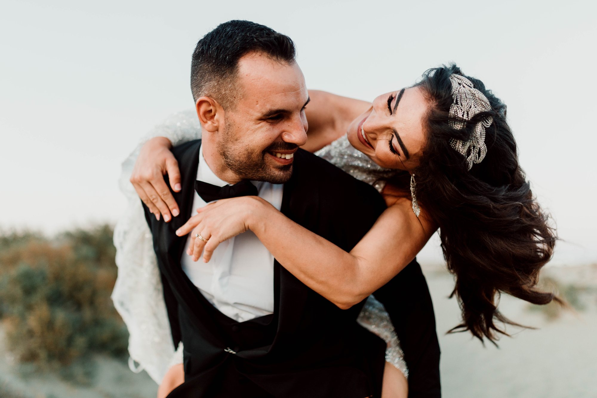 Bride and groom laughing as she wraps her arms around him from behind